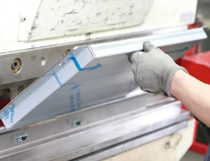 Hände in Handschuhen legen ein Blech an der Abkantpresse an