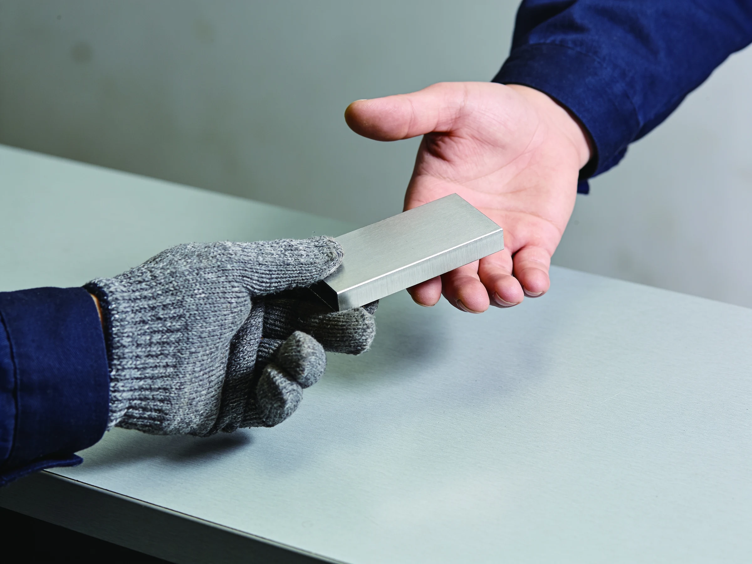 Hand im Arbeitshandschuh reicht ein Bauteil weiter